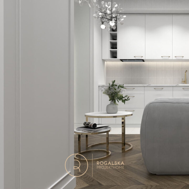 Aneks kuchenny w kolorze biało-kaszmirowym ze złotymi dodatkami. W centrum salonu szara welurowa sofa. Liczne sztukaterie na ścianach dodające mieszkaniu elegancji.